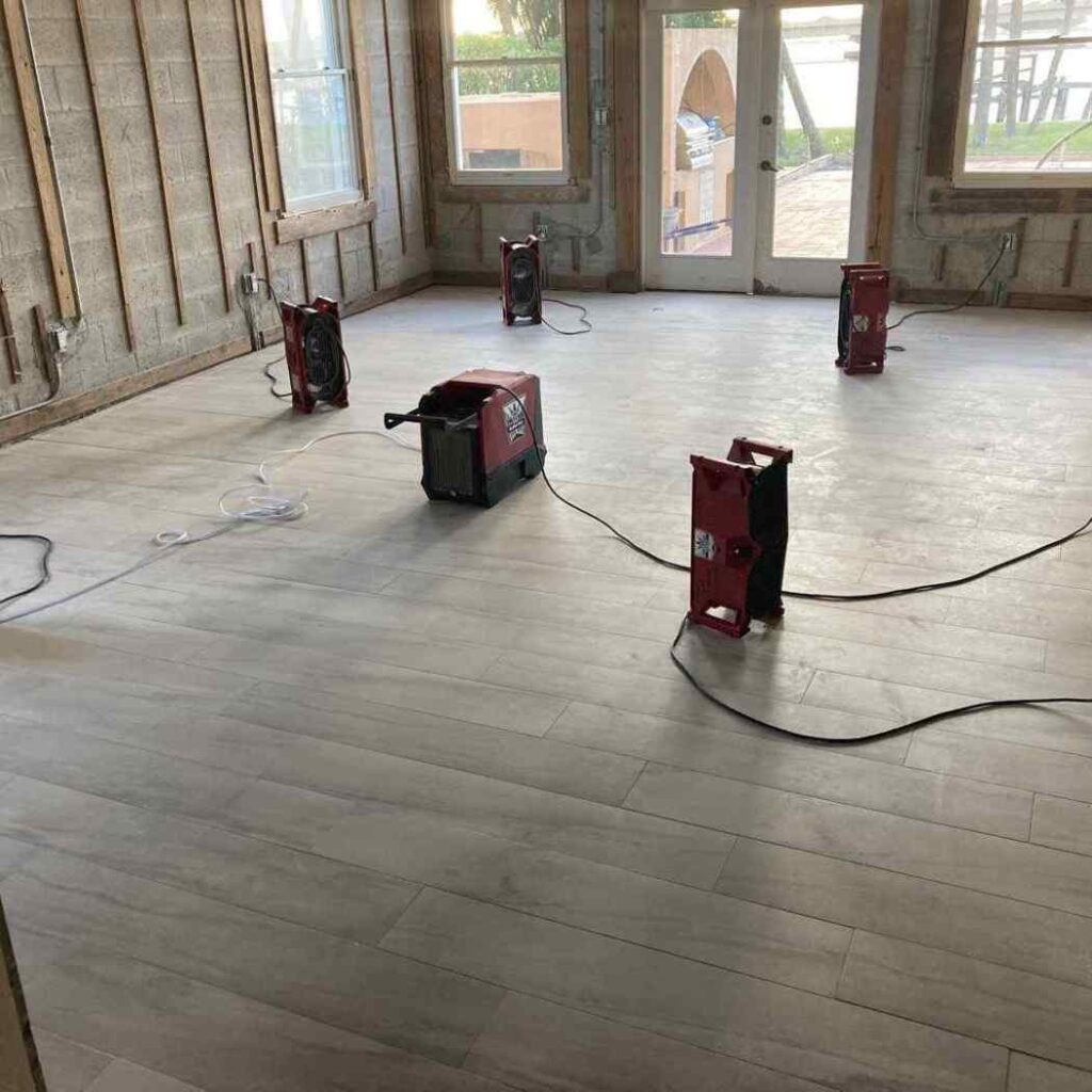 Industrial fans drying a floor in a large room under renovation.